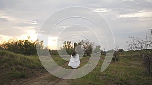 A bride in a wedding dress runs off into the distance on a dirt road, the view from the back is slow-motion.