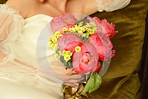 The bride in a white dress with a bright wedding bouquet of pink peonies in her hands