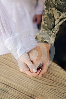 Bride In white dress and groom in military uniform hold each other by the hands