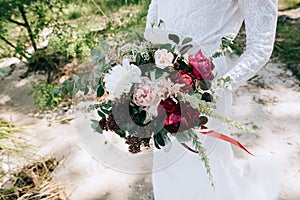 Bride in a white dress holding a beautiful Eucalyptus white pink and red peonies wedding bouquet in her hands