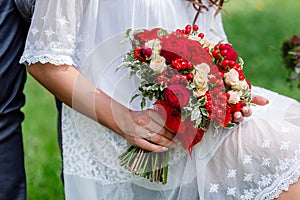 Bride in white dress holding in hands delicate, expensive, trendy bridal wedding bouquet of flowers in marsala and red colors. Clo