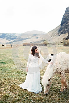 Bride in a white dress strokes the mane of a grazing horse