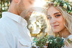 Bride in white dress and wreath and groom portrait in sunny summer day. Rustic outdoor wedding concept