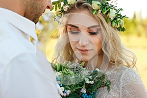 Bride in white dress and wreath and groom portrait in sunny summer day. Rustic outdoor wedding concept