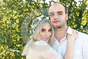 Bride in white dress and wreath and groom portrait in sunny summer day. Rustic outdoor wedding concept