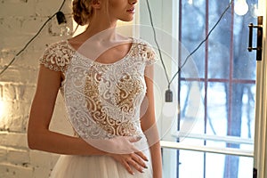 The bride in a white lace dress with embroidered bodice, indoors in loft style.High key. photo
