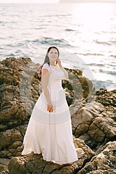 Bride in a white lace dress stands on a rocky seashore by the sea