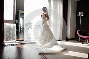 Bride in white lacy wedding dress and veil looking through the window