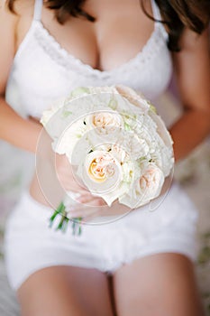 Bride in white lingerie holds a wedding bouquet closeup