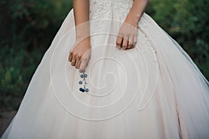A bride in a white lush wedding dress holds in her hand a sprig with blue and light blue round berries.