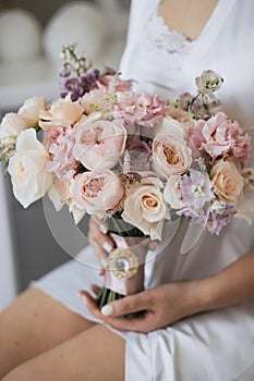 The bride with a white robe holds in her hands a gentle wedding bouquet