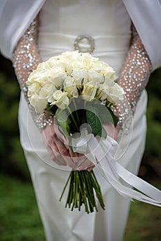 The bride in a white wedding dress is holding a bouquet of white flowers - peonies, roses. Wedding. Bride and groom. Delicate