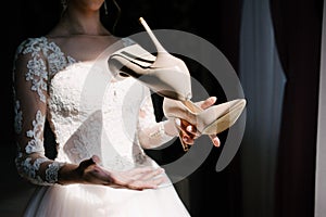 Bride in a white wedding dress holding wedding shoes in her hands