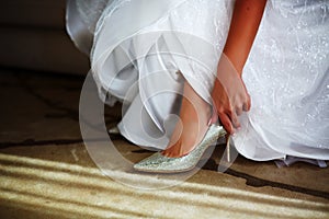 Bride in white wedding dress putting on silver shoes