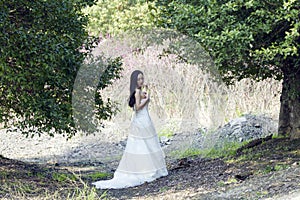 A bride with white wedding dress stand in the middle of trees