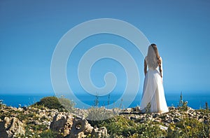 A bride in a white wedding dress standing on a cliff edge looking out to sea
