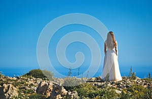 A bride in a white wedding dress standing on a cliff edge looking out to sea