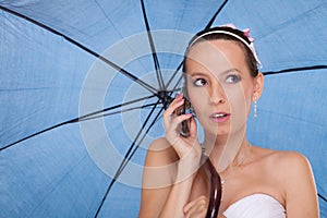 Bride woman with umbrella talking on mobile phone.