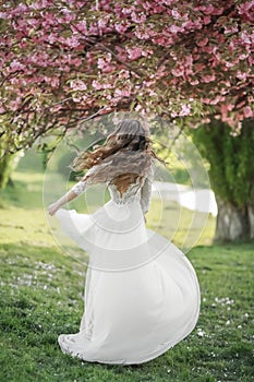 The bride a young woman in a long white dress whirls and dances in a spring Park