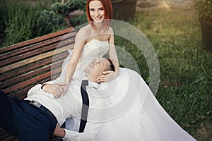 Bridegroom lies on the beautiful girl in a wedding dress in the public park on the bench
