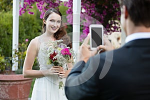 Bridegroom photographing bride holding bouquet at park