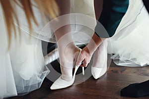 Bridemaid helps bride to put shoes on