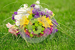 Brides bouquet of colorful flowers lying on a green lawn.