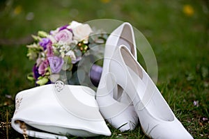 Brides wedding shoes, purs and a bouquet with roses and other flowers on the grass