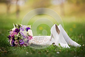 Brides wedding shoes, purs and a bouquet with roses and other flowers on the grass