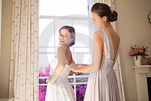 Bridesmaid adjusting bride wedding dress in fitting room