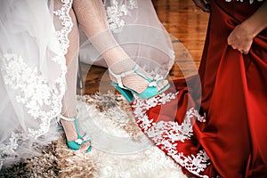 Bridesmaid helps to bride to put wedding shoes.