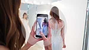 Bridesmaid recording video of bride trying on wedding dress in salon