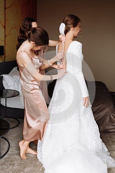 Bridesmaid& x27;s hands helping bride fastens with buttons on the back of a beautiful white wedding lace vintage dress close