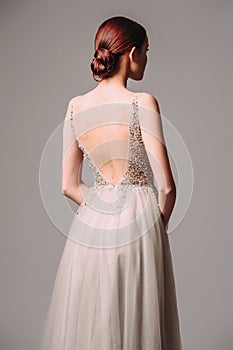 Bridesmaid`s look in dust grey. Beautiful portrait of ginger young woman in summer fluttering dress with shining details on grey b
