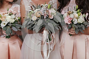 Bridesmaids and bride holding modern wedding bouquets of pink roses and green eucalyptus with pink ribbons. Stylish Contemporary