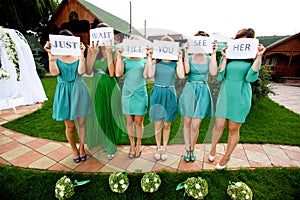 Bridesmaids hold a lettering 'Just wait till you see her' printe