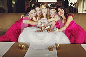 Bridesmaids in pink dresses lean to a pretty bride sitting on th