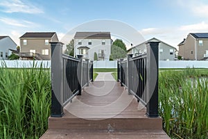 Bridge with brown deck and black guardrails over a pond in front of homes