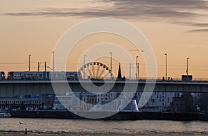 a bridge crosses over water to the ferris wheel behind it