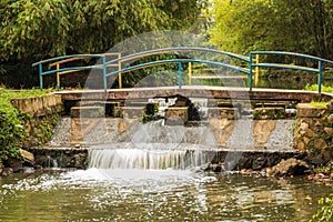 the bridge in the garden over a small dam with foamy water flowing underneath