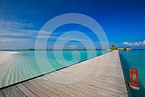 Bridge leading to overwater bungalow in blue lagoon around tropical island in Maldives