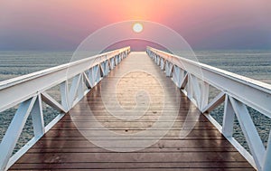 The bridge leads to the sea during sunset.