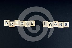 Bridge loans- word composed fromwooden blocks letters on black background, copy space for ad text.