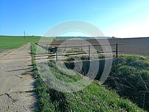 Bridge old with iron railing, across a ditch between a panel road and fields