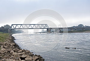 bridge over river ijssel with boats at dutch city of deventer on foggy morning