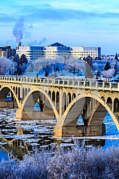 A bridge over a river with snow on the trees and buildings in the background