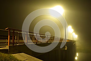 Bridge over the river and the wreathed light of street lamps in heavy fog at night