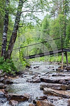 A bridge over a small stream with large rocks in the green forest.