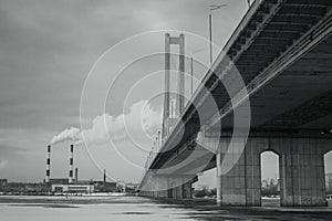 Bridge over the winter frozen river on the background of industrial smoking pipes