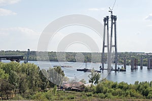 Bridge structure in the city, against a background of green trees, and a cloud. The construction of a bridge in Ukraine, the city